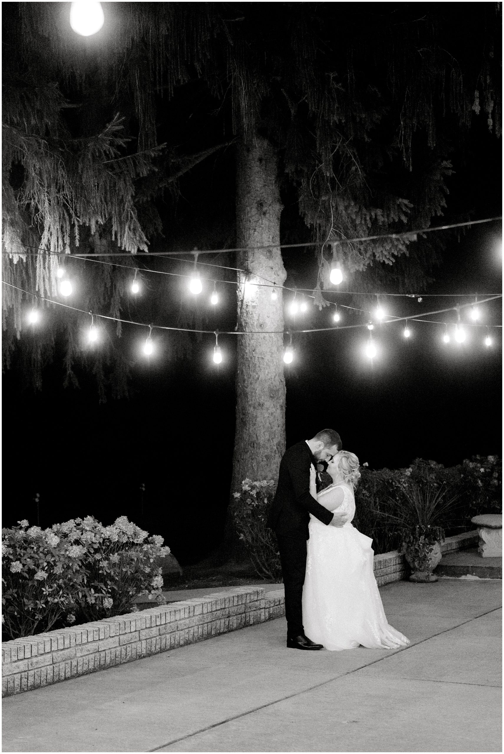 black and white photo of bride and groom dancing under string lights